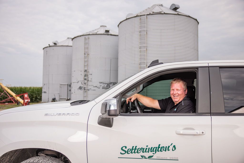 Setterington's employee smiling in work truck with silos in behind